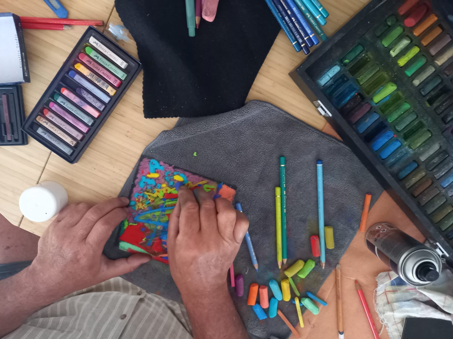 Les mains d’Éric Bailblé travaillant un pastel, entouré de ses craies