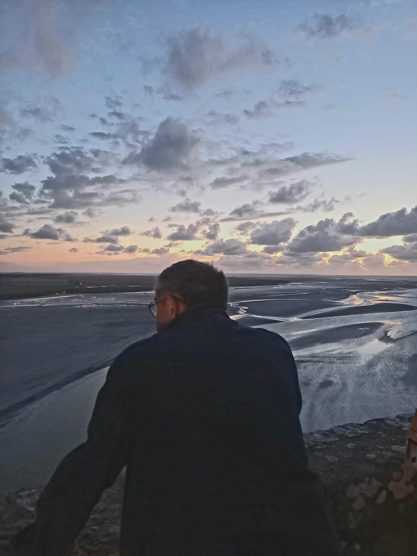 Éric Bailblé de dos, au-dessus de la baie à marée basse, au crépuscule
